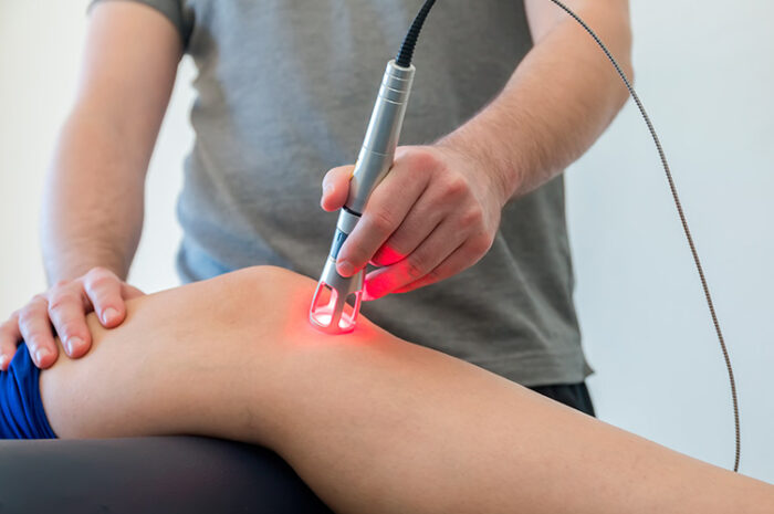 Nell'immagine è presente un fisioterapista che esegue un trattamento di laser terapia appoggiando lo strumento laser sul ginocchio del paziente.